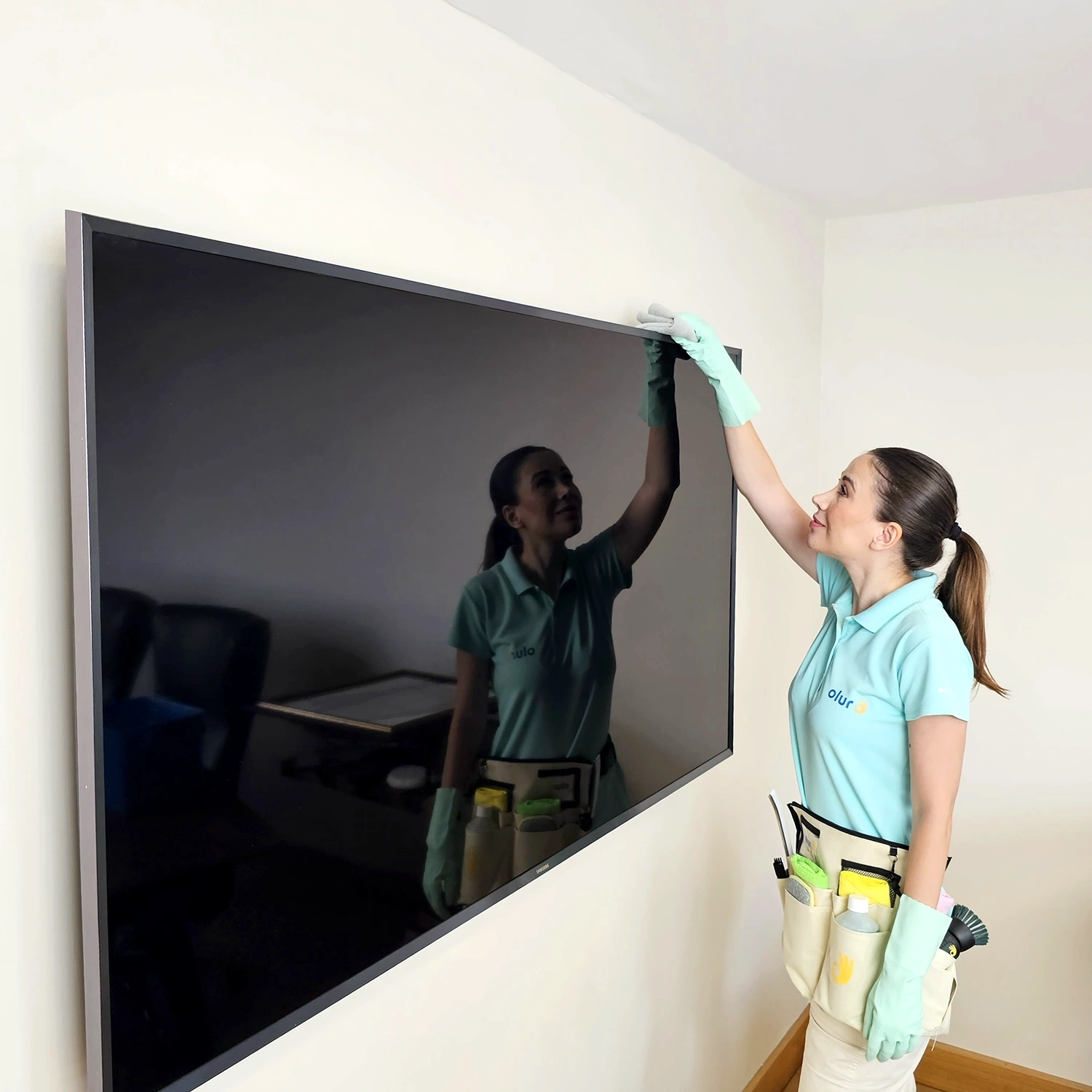 Günlük temizlikçi kadın, ev temizliğinde mikrofiber bez ile televizyonun tozunu alıyor